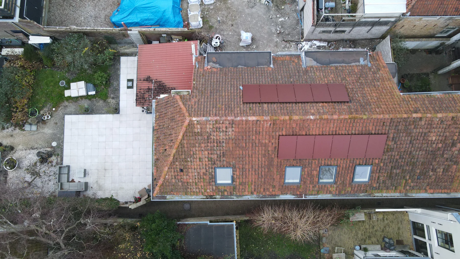 Dakoverzicht met twee velden rode zonnepanelen tussen bestaande dakpannen